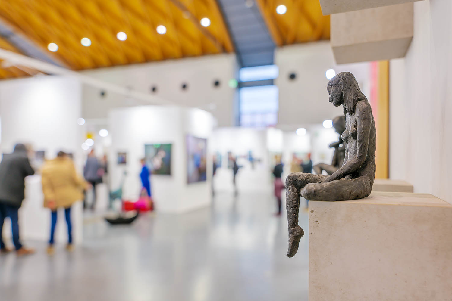 Kleine sitzende Statue schaut auf Messebesucher